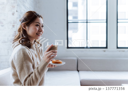 窓辺で飲み物とドーナツを持つ女性 窓辺で飲み物とドーナツを持つ女性 137771356
