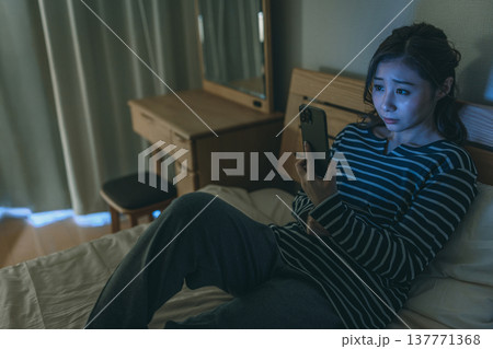 暗い部屋でスマホの光を見る女性 暗い部屋でスマホの光を見る女性 137771368