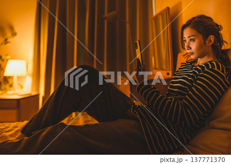 夜の寝室でスマホを操作する女性 137771370