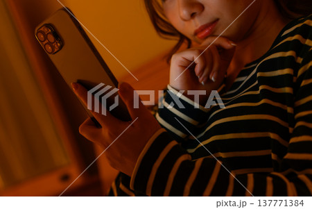 ベッドでスマホを操作する女性の手元 137771384