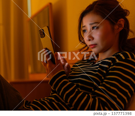 ベッドでスマホを見て考え込む女性 137771398
