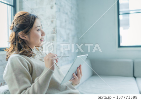 窓辺でタブレットを見る女性の横顔 137771399