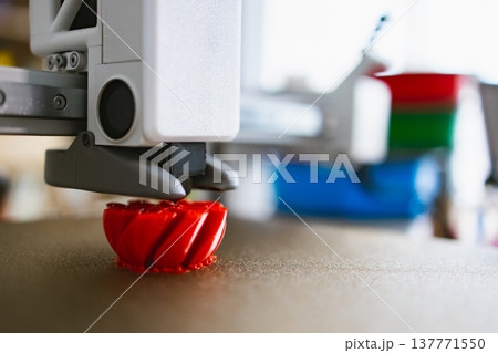 A close-up view of a 3D printer nozzle depositing molten red plastic to build a complex object layer by layer A close-up view of a 3D printer nozzle depositing molten red plastic to build a complex object layer by layer 137771550
