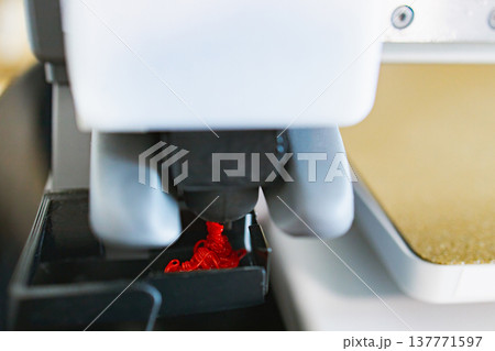 Close-up view of a 3D printer nozzle depositing molten red filament onto a build plate, showcasing the additive manufacturing process 137771597