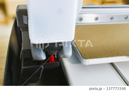 Close-up view of a 3D printer's nozzle depositing molten red filament onto a build plate, showcasing the additive manufacturing process 137771598