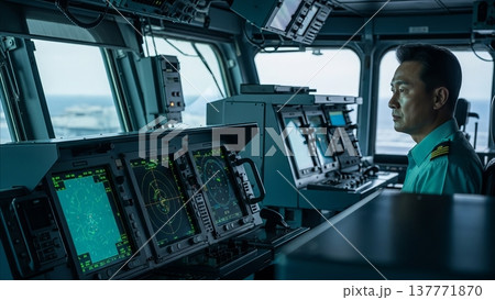 Asian naval officer monitoring radar systems and navigation equipment on modern warship bridge during maritime operations 137771870
