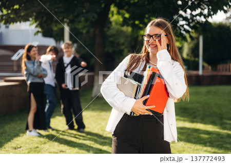 Bunch of notepads in hands of a girl. Group of students are near university together Bunch of notepads in hands of a girl. Group of students are near university together 137772493
