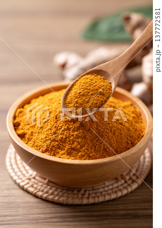 Turmeric powder in a wooden bowl with a wooden spoon scooping it, and fresh turmeric roots  137772581