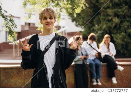 Young guy is standing in front of his friends. Group of students are near university together Young guy is standing in front of his friends. Group of students are near university together 137772777