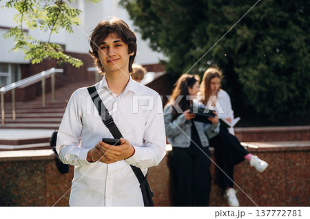 Young guy is standing in front of his friends. Group of students are near university together Young guy is standing in front of his friends. Group of students are near university together 137772781