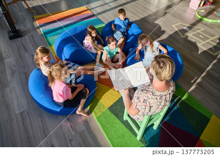 Teacher reading story to children during classroom circle time on colorful rug and bean bags 137773205