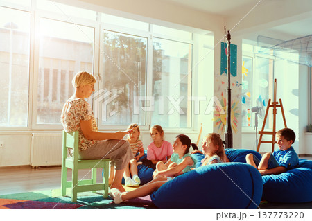 Teacher reading a story to attentive children during cozy classroom story time in a bright kindergarten Teacher reading a story to attentive children during cozy classroom story time in a bright kindergarten 137773220