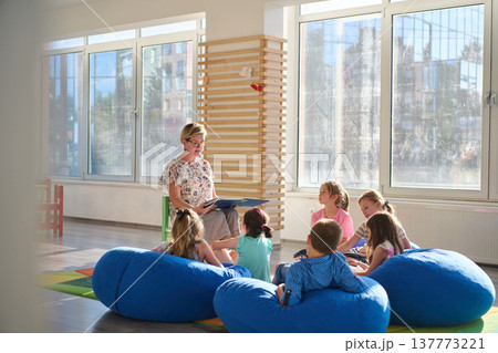 Female teacher reading to young children during storytime in a bright classroom seating area Female teacher reading to young children during storytime in a bright classroom seating area 137773221