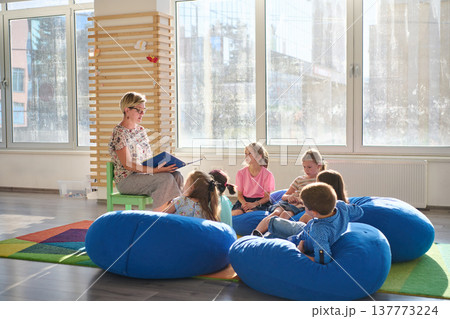 Teacher reading a picture book to young children during cozy classroom circle time on bean bags 137773224