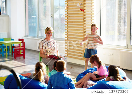 Teacher reading to children during storytime in bright preschool classroom with kids laughing and learning Teacher reading to children during storytime in bright preschool classroom with kids laughing and learning 137773305