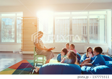Teacher reading a story to young children during group storytime in a bright classroom Teacher reading a story to young children during group storytime in a bright classroom 137773311