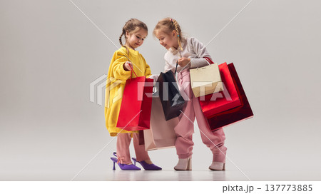 Two little girls smiling while checking shopping bags and wearing oversized colorful fashion clothes 137773885