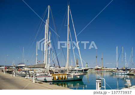 A horizontal shot of white luxury yachts and motorboats docked at a pier in a turquoise sea bay under a clear blue sky. 137773937