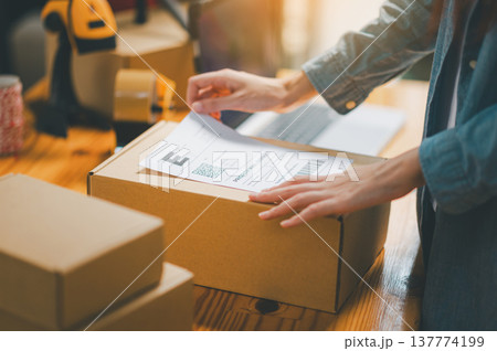 startup young female small business owners attaching shipping labels to cardboard boxes or parcels for delivery of customer orders-concept shopping online. startup young female small business owners attaching shipping labels to cardboard boxes or parcels for delivery of customer orders-concept shopping online. 137774199