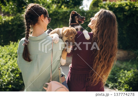 Rear view of two women that are standing and holding dogs in hands Rear view of two women that are standing and holding dogs in hands 137774278