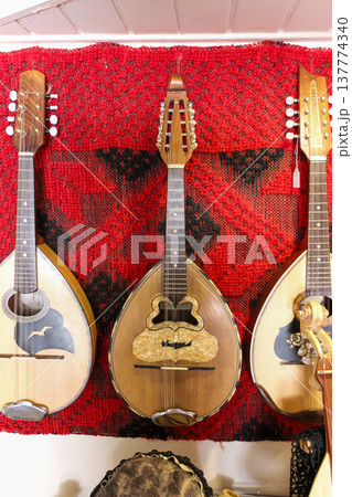 Traditional handmade mandolins and Cretan bulgari on a red woven rug 137774340