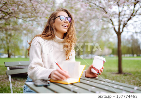 Cute woman in glasses writes in notepad, sits with laptop enjoying sunny spring day. Relax concept. 137774465