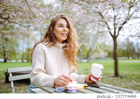 Cute woman in glasses writes in notepad, sits with laptop enjoying sunny spring day. Relax concept. 137774466