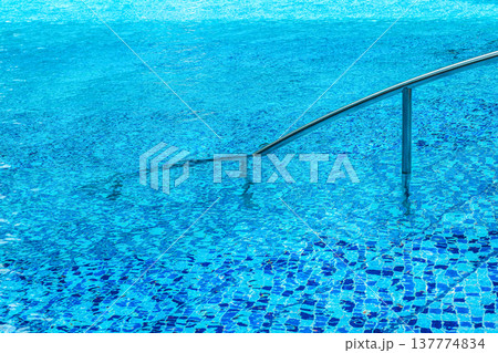 Swimming pool with blue water and stainless steel handrail visible 137774834