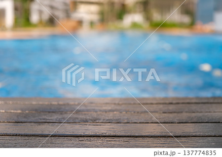 Wooden deck edge overlooking a swimming pool with blue water background Wooden deck edge overlooking a swimming pool with blue water background 137774835