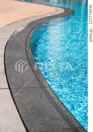 Curved stone edge of swimming pool with clear blue water surface Curved stone edge of swimming pool with clear blue water surface 137774836