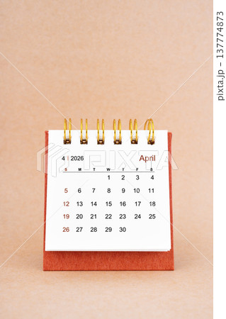 April 2026 white desk calendar on brown background. 137774873