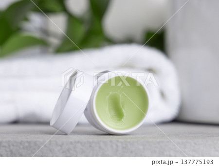 Opened balm jar with natural herbal salve near green leaves in white bathroom, skincare product 137775193