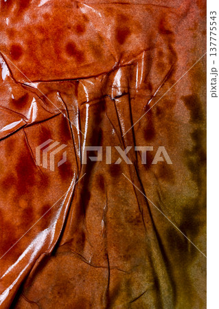 An abstract macro shot of a glossy, burnt orange and brown surface featuring heavy wrinkles, deep creases, and subtle reflections. Ideal for rustic or industrial backgrounds 137775543