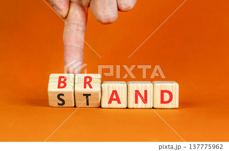 Brand or stand symbol. Concept words Brand Stand on beautiful wooden blocks. Beautiful orange background. Businessman's hand. Business brand or stand concept. Copy space. Brand or stand symbol. Concept words Brand Stand on beautiful wooden blocks. Beautiful orange background. Businessman's hand. Business brand or stand concept. Copy space. 137775962
