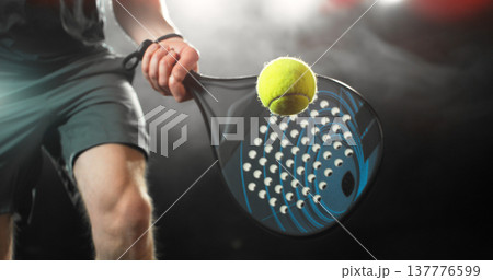 Dynamic action shot of a padel player hitting a yellow ball with a racket during a match. Dramatic lighting highlights movement, speed and power, capturing the energy and intensity of modern racket Dynamic action shot of a padel player hitting a yellow ball with a racket during a match. Dramatic lighting highlights movement, speed and power, capturing the energy and intensity of modern racket 137776599