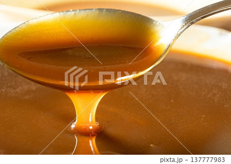 Sweet caramel sauce dripping from spoon, liquid caramel close-up. Sweet caramel sauce dripping from spoon, liquid caramel close-up. 137777983