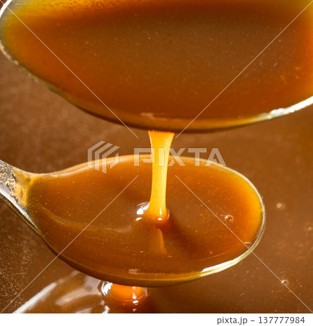 Caramel sauce in a spoon close-up, liquid caramel texture, sweet topping. Caramel sauce in a spoon close-up, liquid caramel texture, sweet topping. 137777984