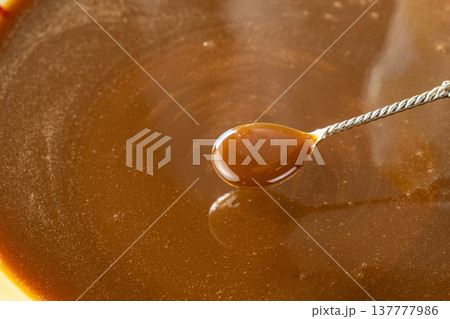 Caramel sauce in a spoon close-up, liquid caramel texture, sweet topping. Caramel sauce in a spoon close-up, liquid caramel texture, sweet topping. 137777986