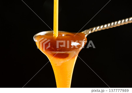 Liquid caramel sauce dripping from silver spoon. Liquid caramel sauce dripping from silver spoon. 137777989