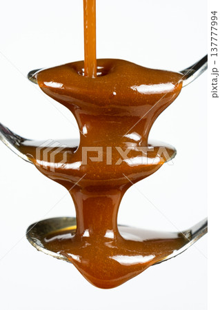Flowing stream of liquid caramel on white background. 137777994