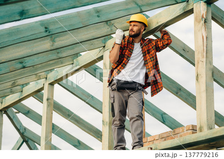 Giving orders by using walkie talkie. Construction worker is on the roof of a house Giving orders by using walkie talkie. Construction worker is on the roof of a house 137779216