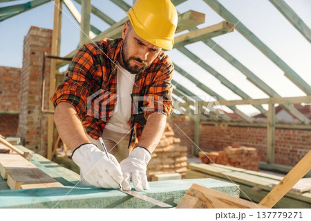 Measuring and marking the plank. Construction worker is on the roof of a house 137779271