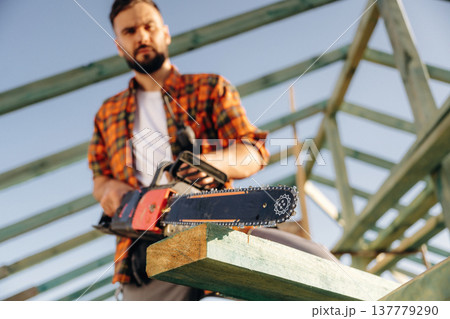 Front view, with chainsaw. Construction worker is on the roof of a house 137779290