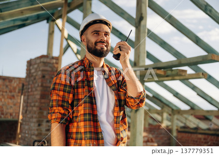 Talking by using walkie talkie. Construction worker is on the roof of a house Talking by using walkie talkie. Construction worker is on the roof of a house 137779351