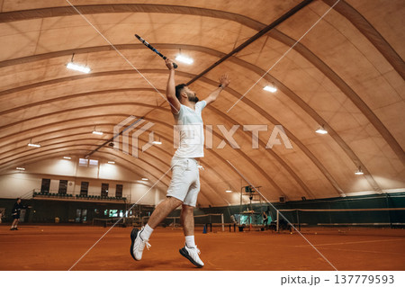 Jumping, photo in action. Man is playing tennis indoors in the hangar 137779593