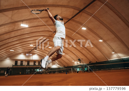 In the air, jumping. Man is playing tennis indoors in the hangar 137779596