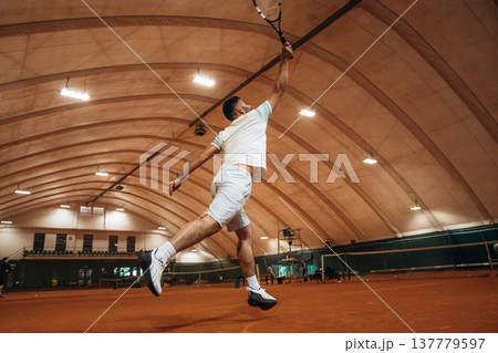 In the air, jumping. Man is playing tennis indoors in the hangar 137779597