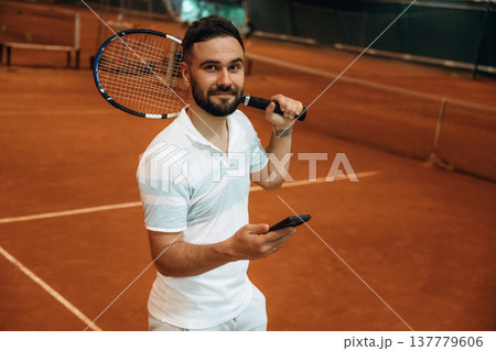 Smartphone is in hand. Man is playing tennis indoors in the hangar Smartphone is in hand. Man is playing tennis indoors in the hangar 137779606