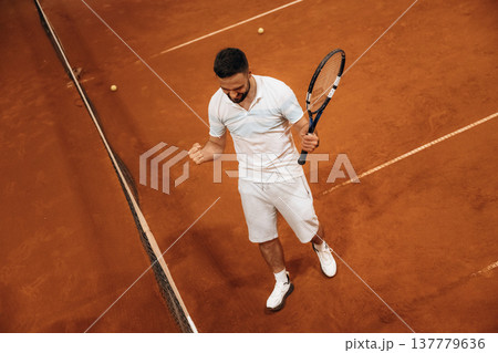 Celebrating victory, happy face. Man is playing tennis indoors in the hangar Celebrating victory, happy face. Man is playing tennis indoors in the hangar 137779636