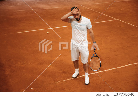 In white sport clothes. Man is playing tennis indoors in the hangar In white sport clothes. Man is playing tennis indoors in the hangar 137779640